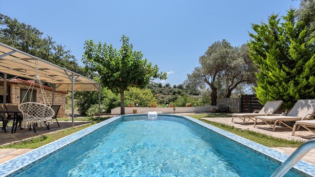 Una piscina rectangular con borde de azulejos, rodeada de sillones de descanso y una zona de estar techada.