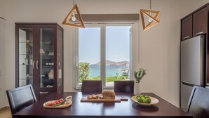 Uma área de refeições moderna com vista para o mar, uma mesa de madeira, cadeiras escuras e um armário de vidro.