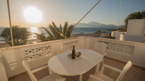 Een witte tafel met stoelen op een balkon met uitzicht op een strand en bergen op de achtergrond.