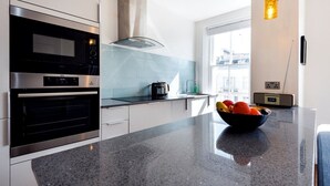 A modern kitchen with a black countertop, stainless steel appliances, and a bowl of fruit.