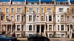 A row of terraced houses with bay windows, a black car parked in front, and a clear blue sky.