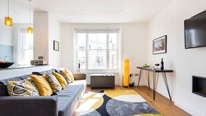 A modern living room with a grey sofa, a yellow rug, a standing lamp, and a TV mounted on the wall.