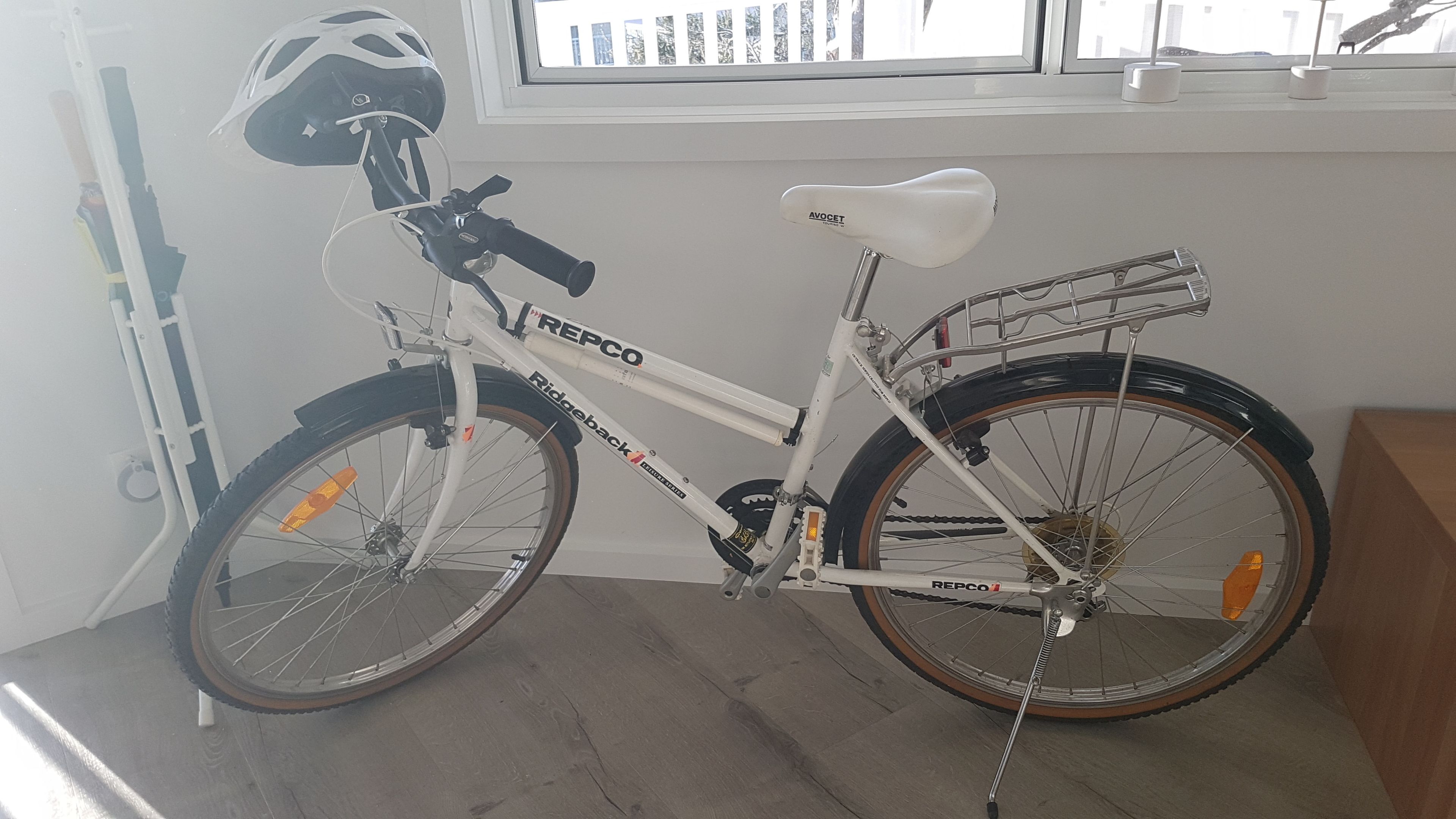A white bicycle with a basket and a seat, parked indoors.