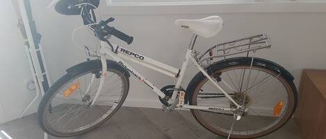 A white bicycle with a basket and a seat, parked indoors.