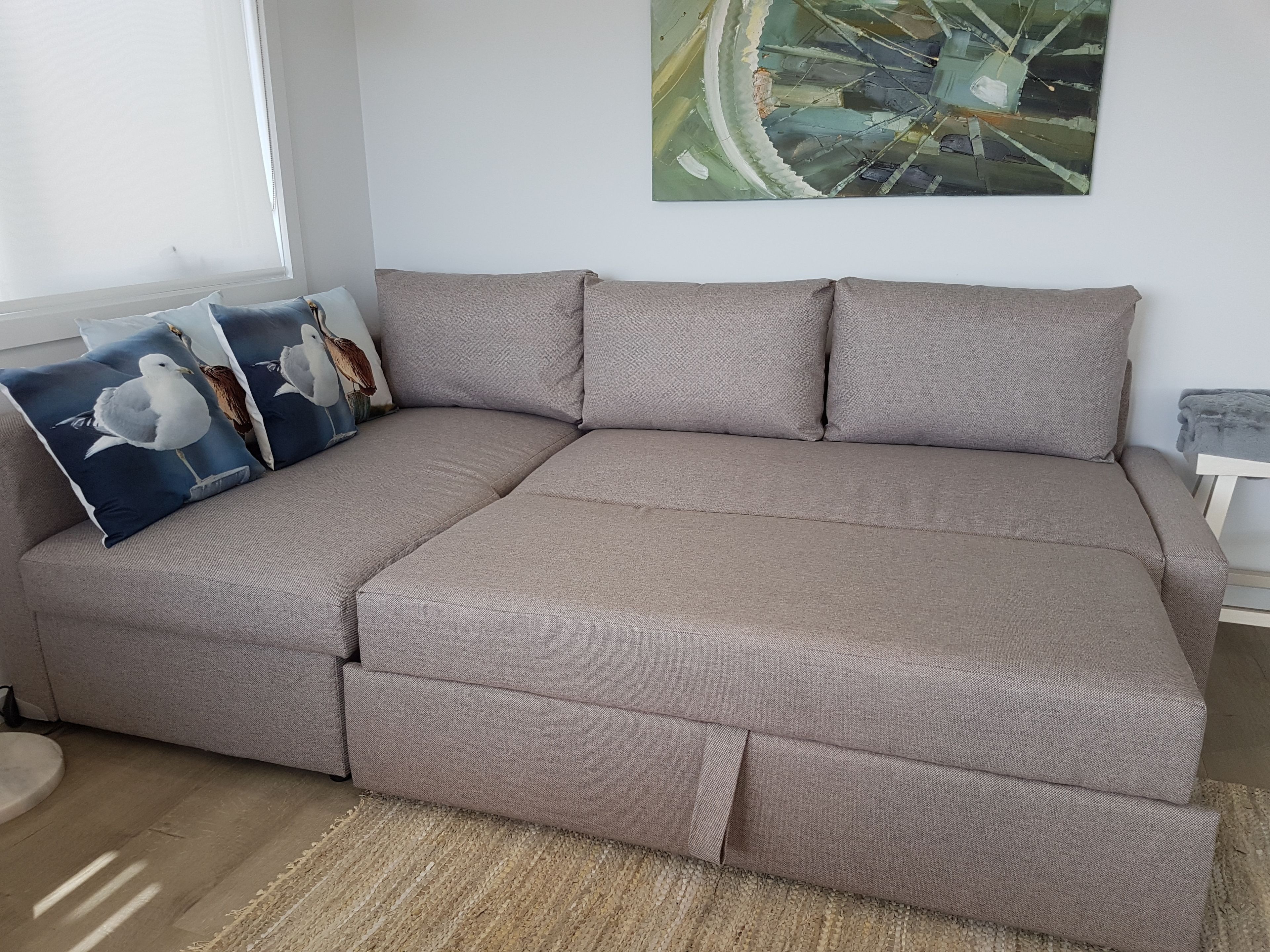 Ein modulares Sofa mit grauem Stoffbezug, ein gewebter Teppich und ein Bild an der Wand.