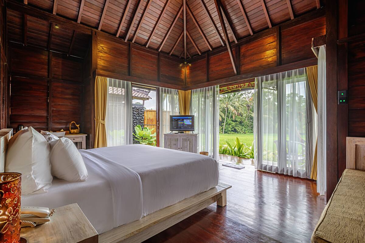 Une chambre spacieuse avec un grand lit, un plafond en bois et un téléviseur posé sur une commode blanche.