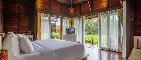 A spacious bedroom with a large bed, wooden ceiling, and a TV on a white cabinet.