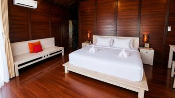 Une chambre d’hôtel avec un plancher en bois, un lit avec une literie blanche, un banc avec des coussins, des lampes de chevet et un appareil de climatisation.