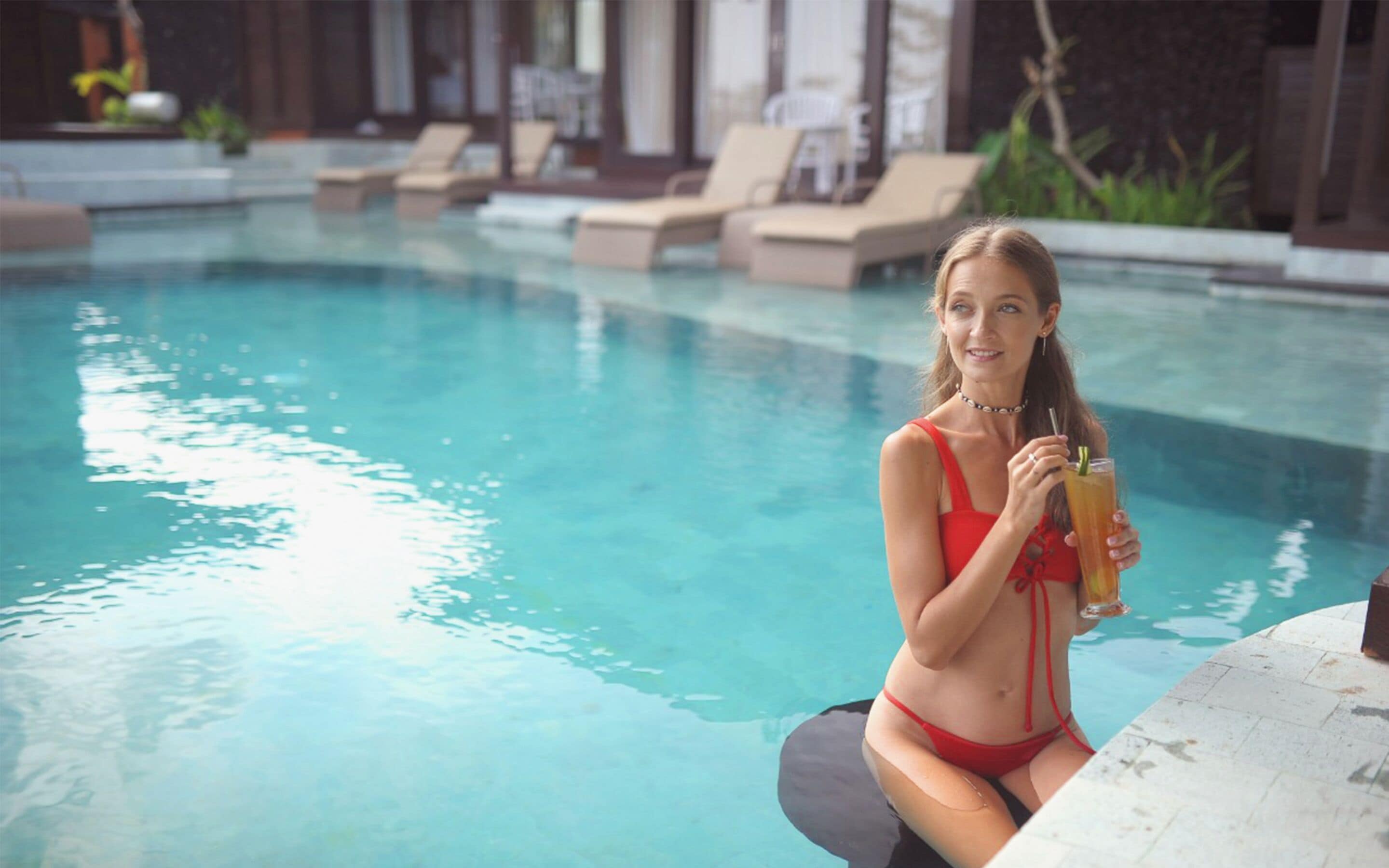 A person sitting by a pool with lounge chairs and a clear blue pool.