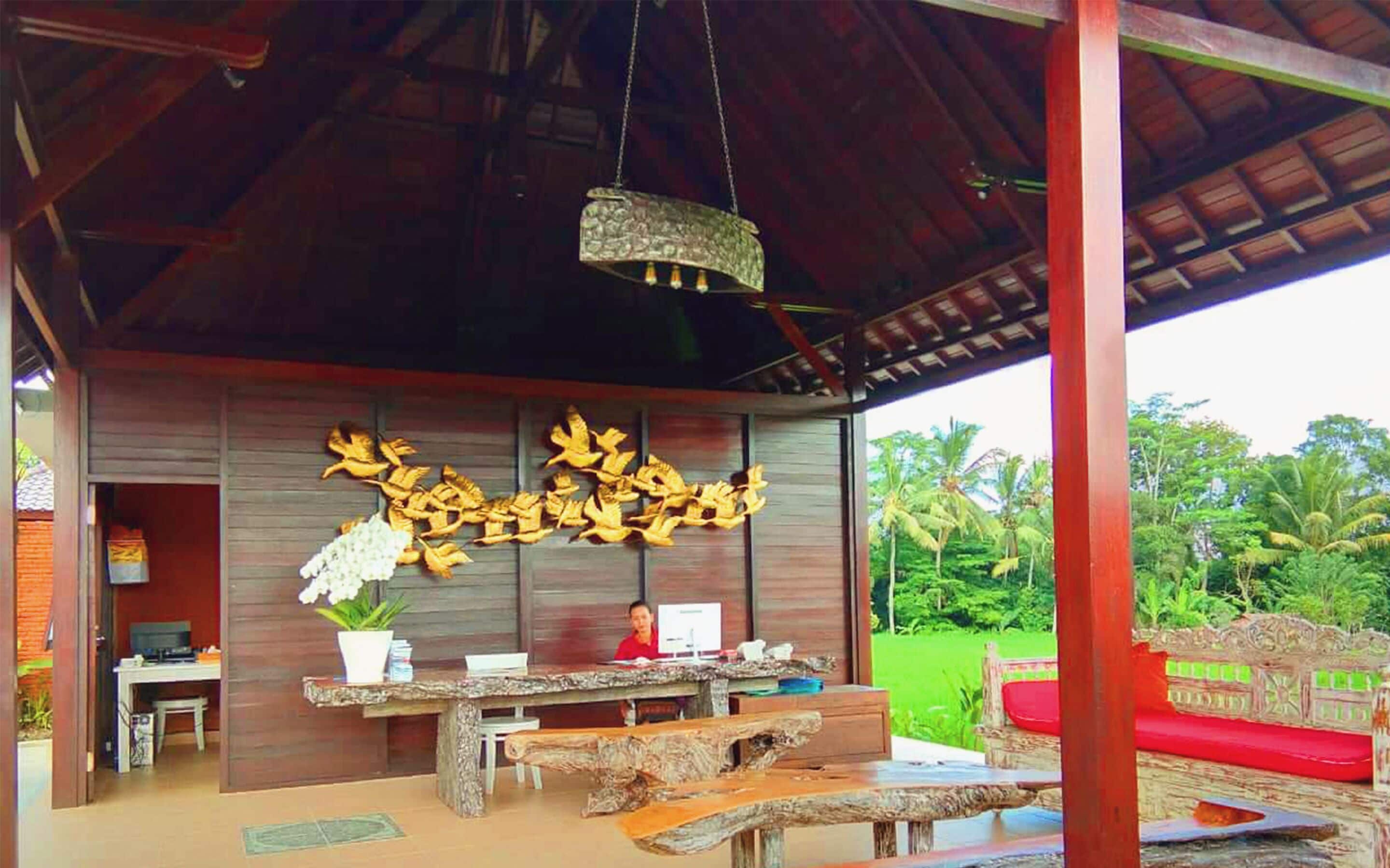A covered outdoor area with a wooden table and benches, a hanging light fixture, and a wall with decorative elements.