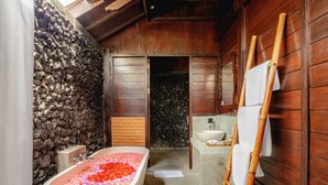 Een badkamer met een stenen muur, een houten vloer, een bad vol rozenblaadjes, een houten ladder en een wastafel.