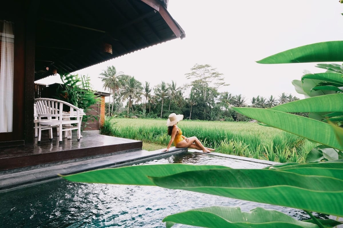Une femme est assise au bord d’une piscine, avec un paysage verdoyant luxuriant en arrière-plan.