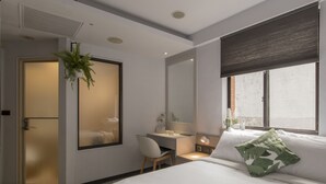 A modern hotel room with a bed, a desk, a chair, a plant, and a window with a view. - Peng Apartment (Taipei)