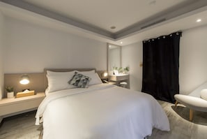 A modern bedroom with a large bed, bedside table, lamp, and a chair. - Peng Apartment (Taipei)