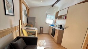 Ein kompakter Wohnbereich mit einer Couch, einem kleinen Esstisch, einer Küchenzeile und einem Fenster, das für natürliches Licht sorgt.