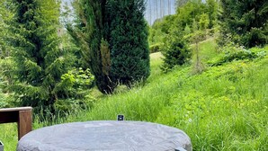 Ein Whirlpool auf einer Holzterrasse mit Blick auf eine grüne Hügelkuppe und Bäume.