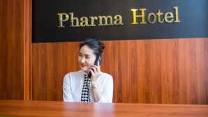 Ein Empfangsschalter mit einem Schild, auf dem in goldener Schrift auf schwarzem Grund 'Pharma Hotel' steht.