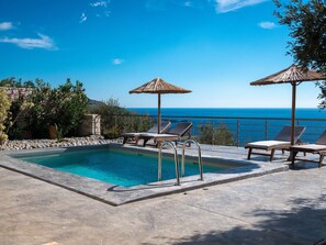 A pool with lounge chairs and umbrellas, overlooking a clear blue sea.