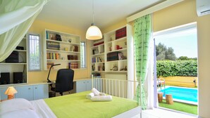 A bedroom with a bed, a desk, a chair, a bookshelf, and a view of a swimming pool.