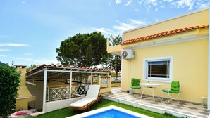 A backyard with a swimming pool, a covered patio area, and a small table with chairs.