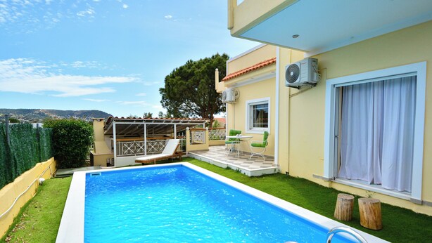 A swimming pool with a clear blue water, surrounded by a well-maintained lawn and a patio area with outdoor furniture.