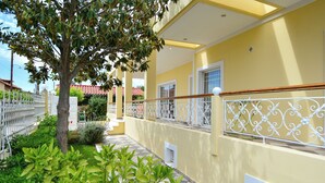A yellow building with a white railing, a tree, and green plants.