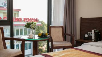 Une chambre d’hôtel avec un lit, deux chaises, une petite table sur laquelle se trouvent un vase, des pommes et une tasse.