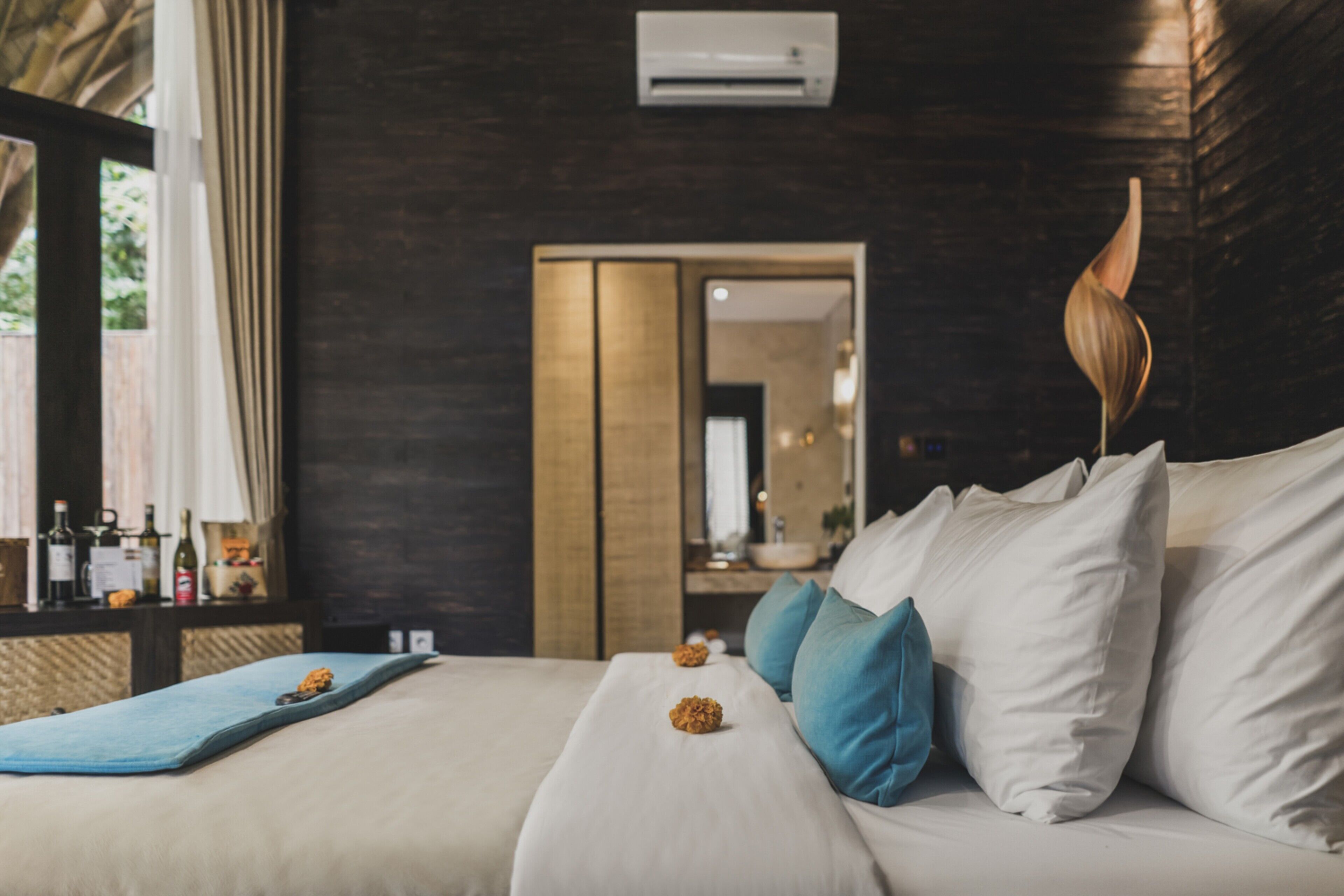 Una habitación de hotel moderna con una cama, almohadas, una mesita de noche con botellas y un espejo.