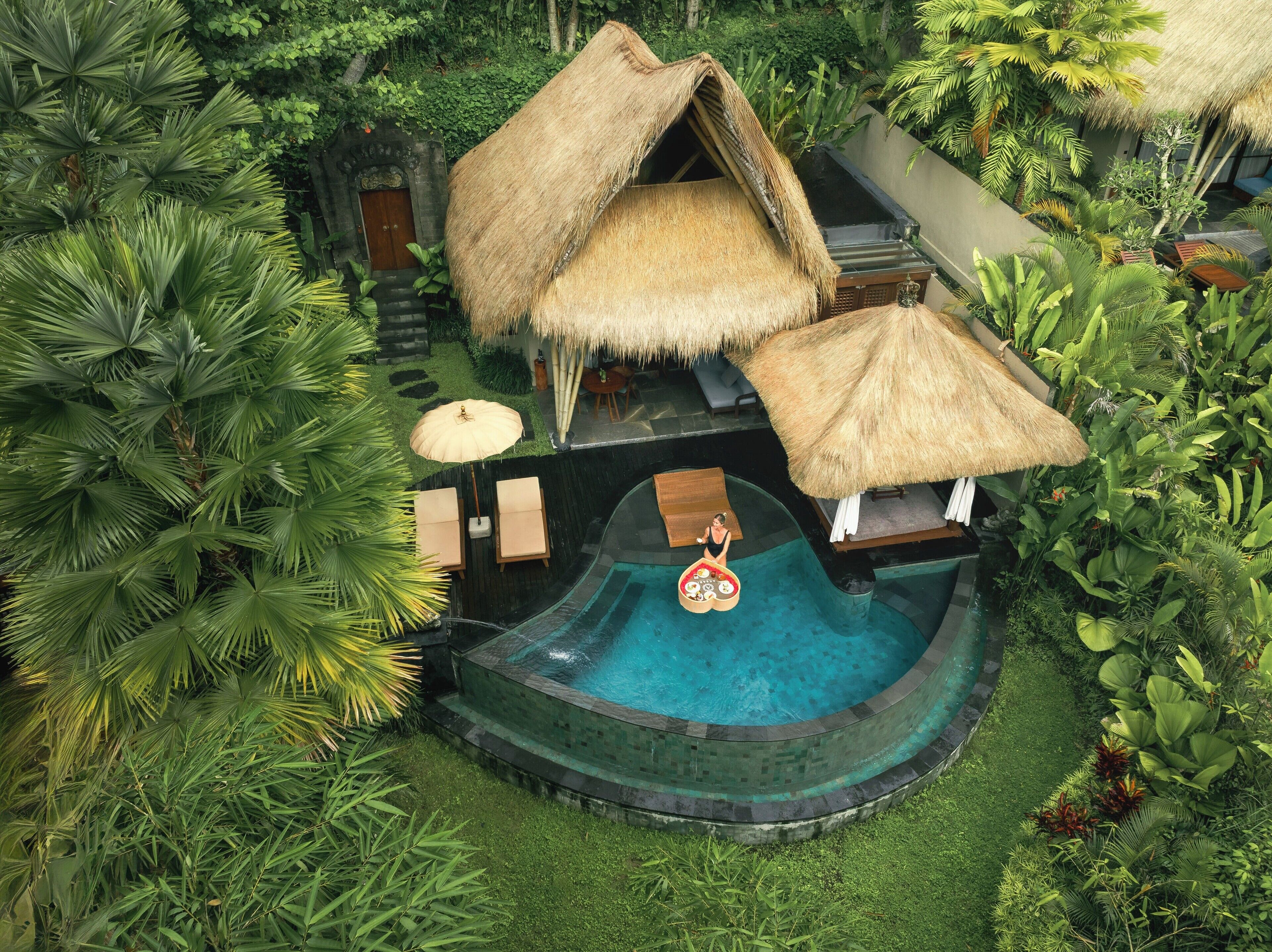 Ein tropisches Resort mit einer strohgedeckten Struktur, einem Swimmingpool und üppiger Vegetation.