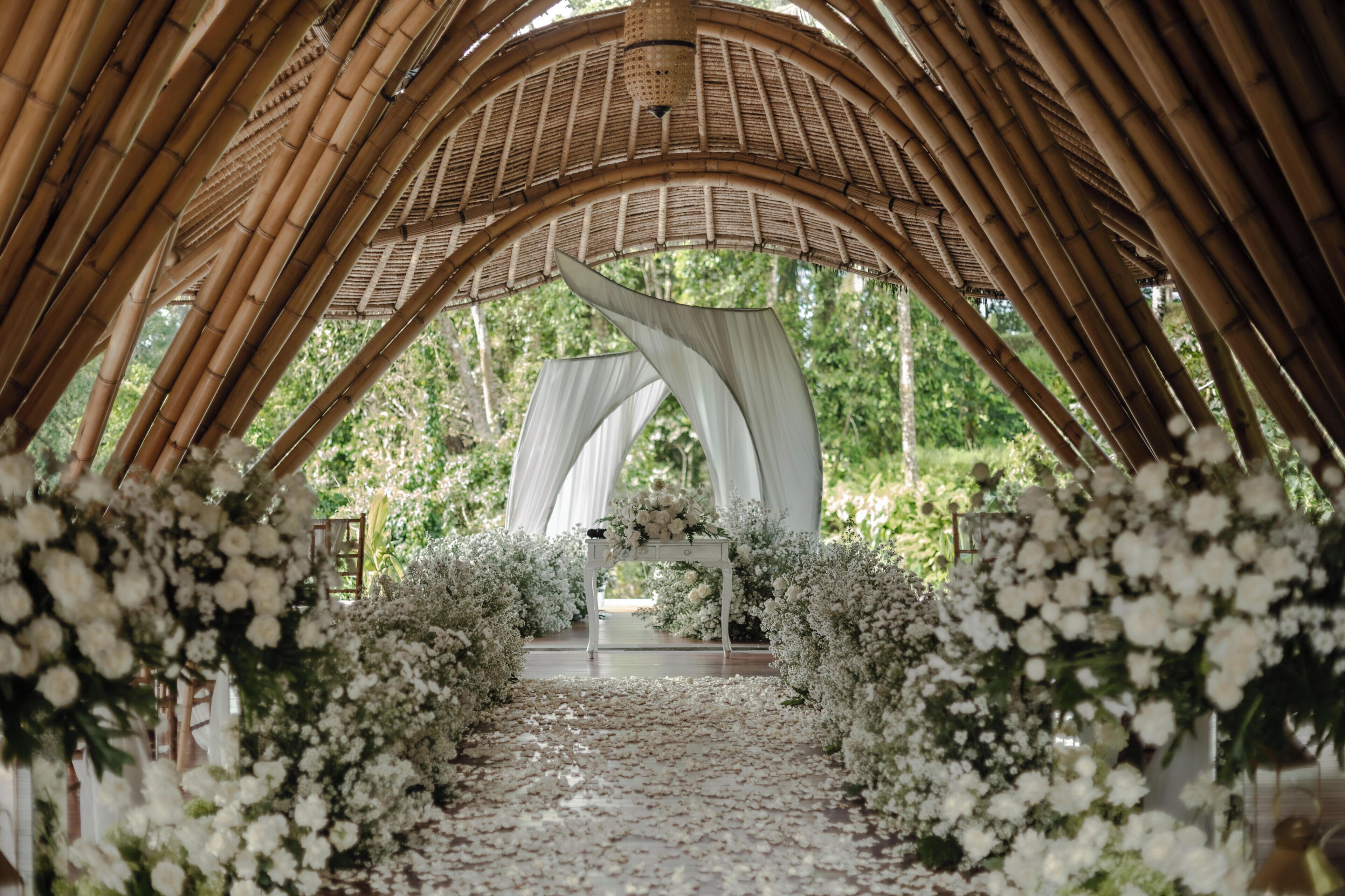 An arched bamboo structure with a white table and floral decorations.