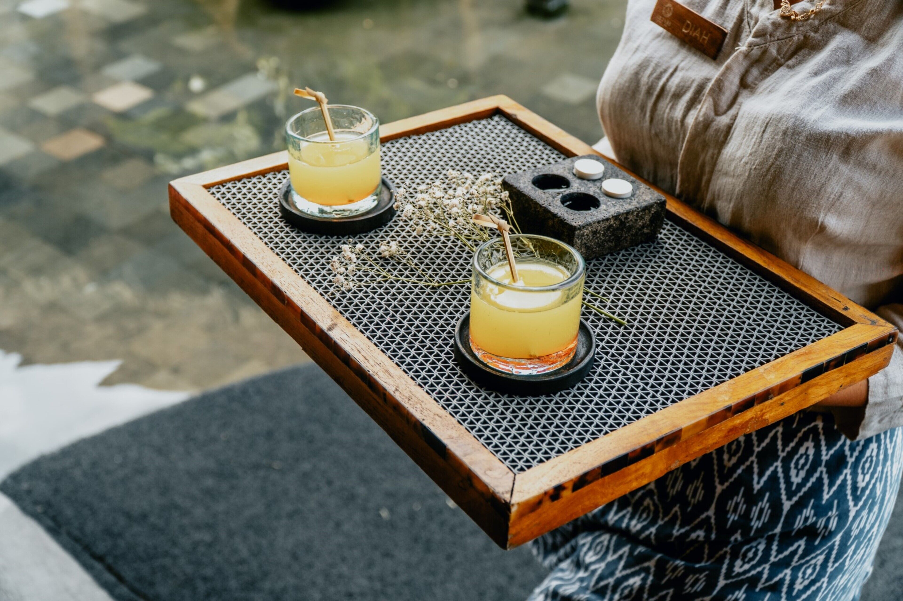 A tray with two glasses of a yellow beverage, a stone with holes, and a small wooden block.