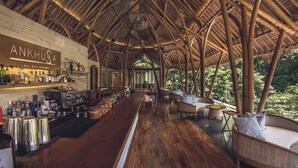 A bamboo-roofed bar area with a bar counter, seating, and a view of greenery.