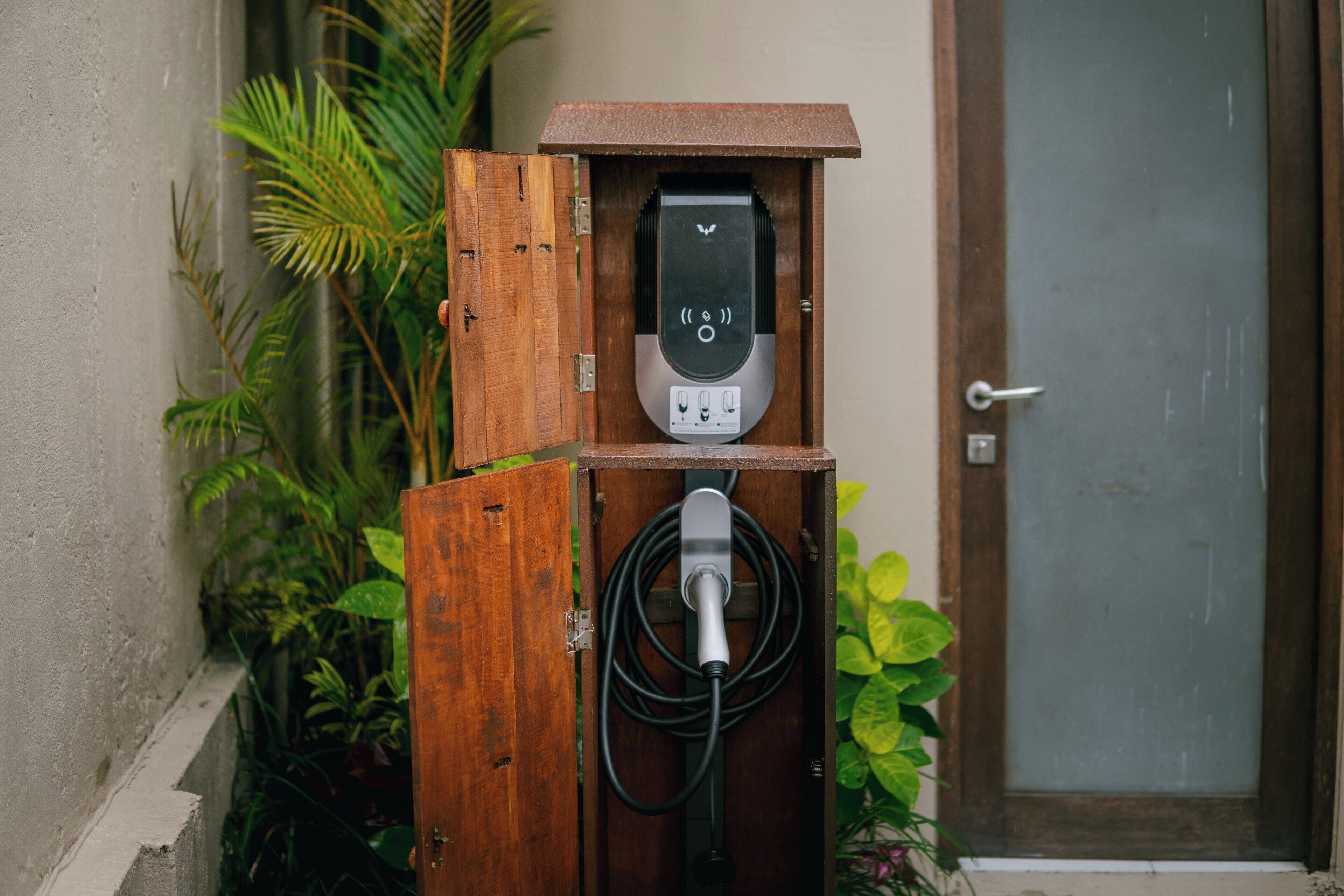 An electric vehicle charging station with a wooden enclosure, a digital display, and a cable connected to a vehicle.