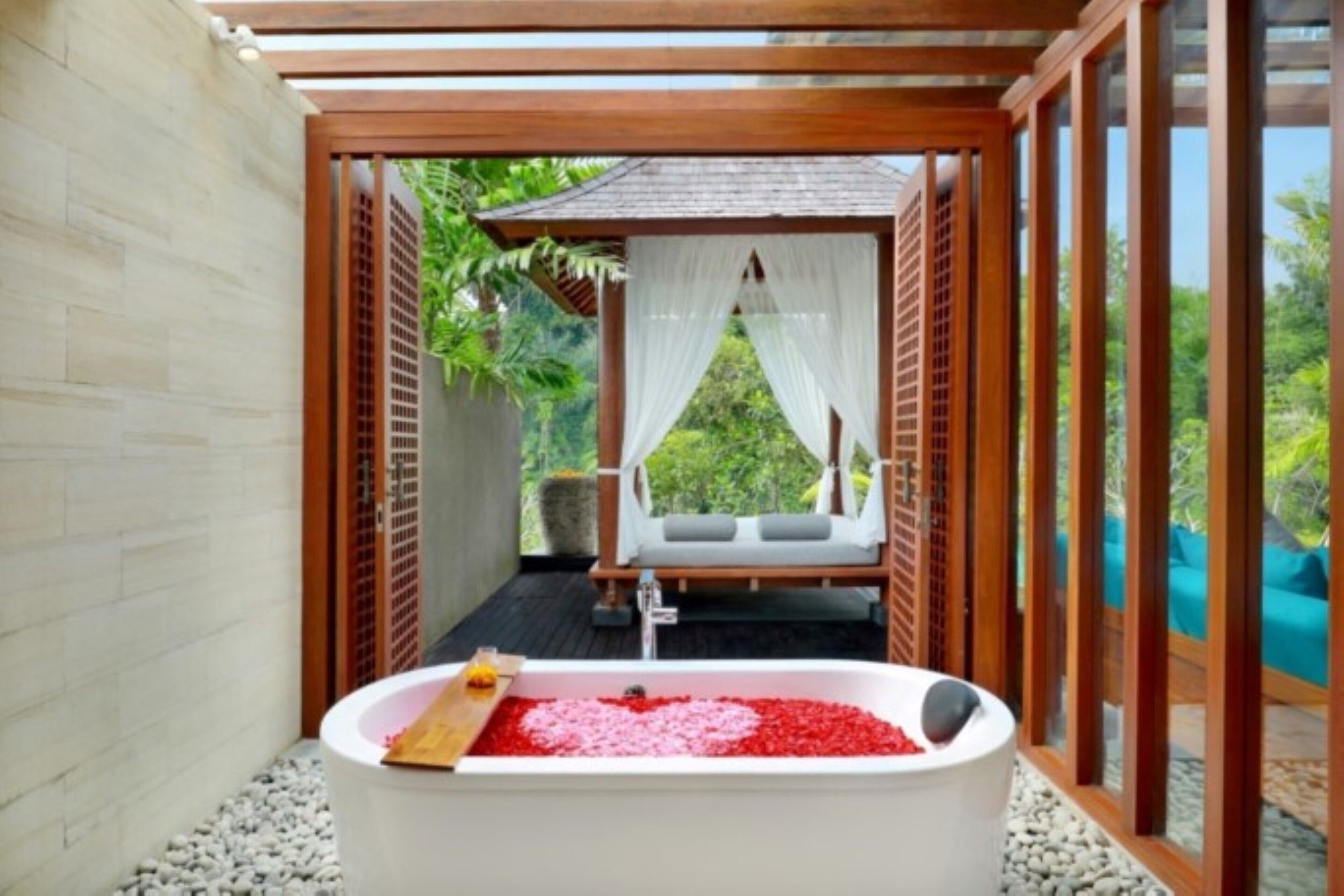 A spa area with a bathtub filled with red pebbles, a wooden bench, and a view of greenery.