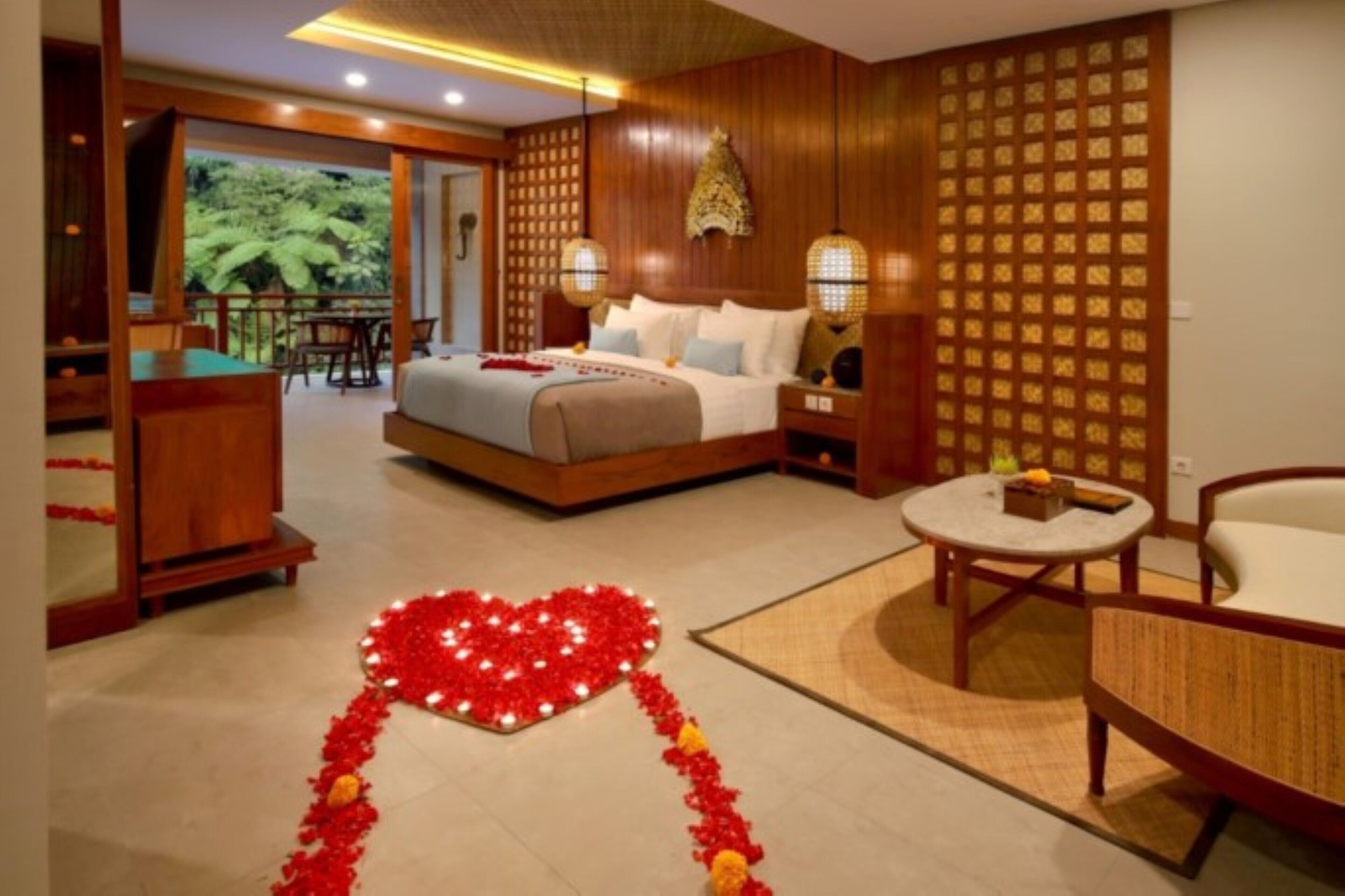Une chambre d’hôtel avec un lit, un bureau, un coin repas et un arrangement floral en forme de cœur posé sur le sol.