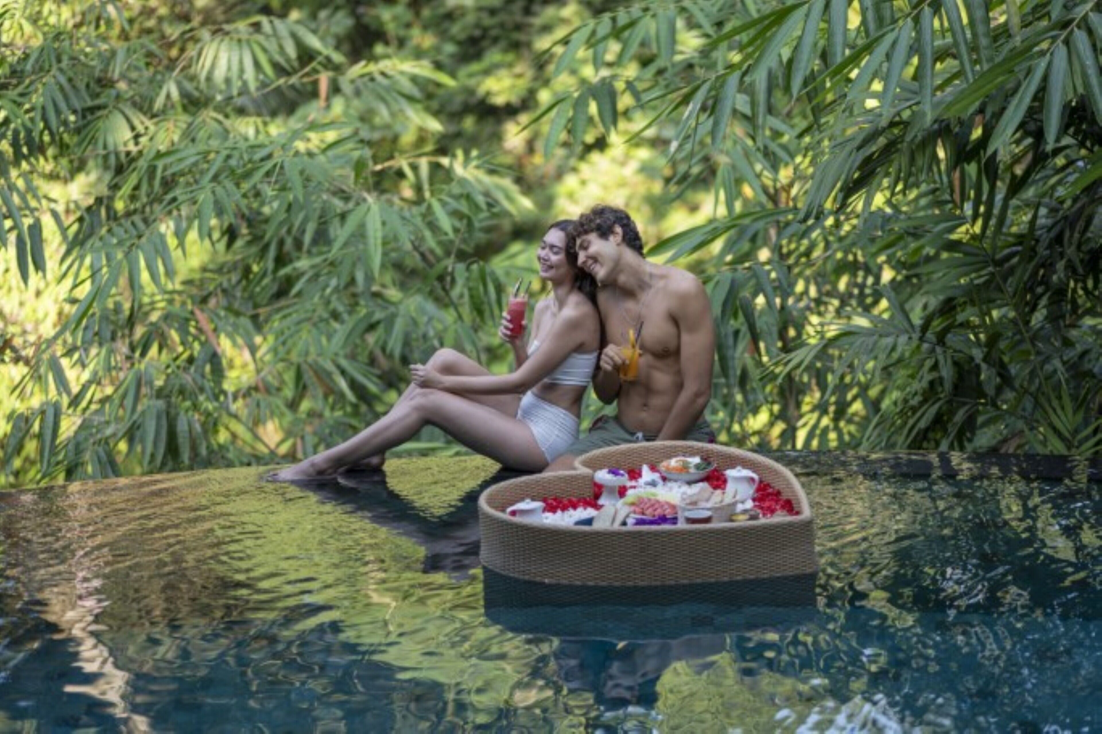 A couple sitting by a pool surrounded by lush greenery.