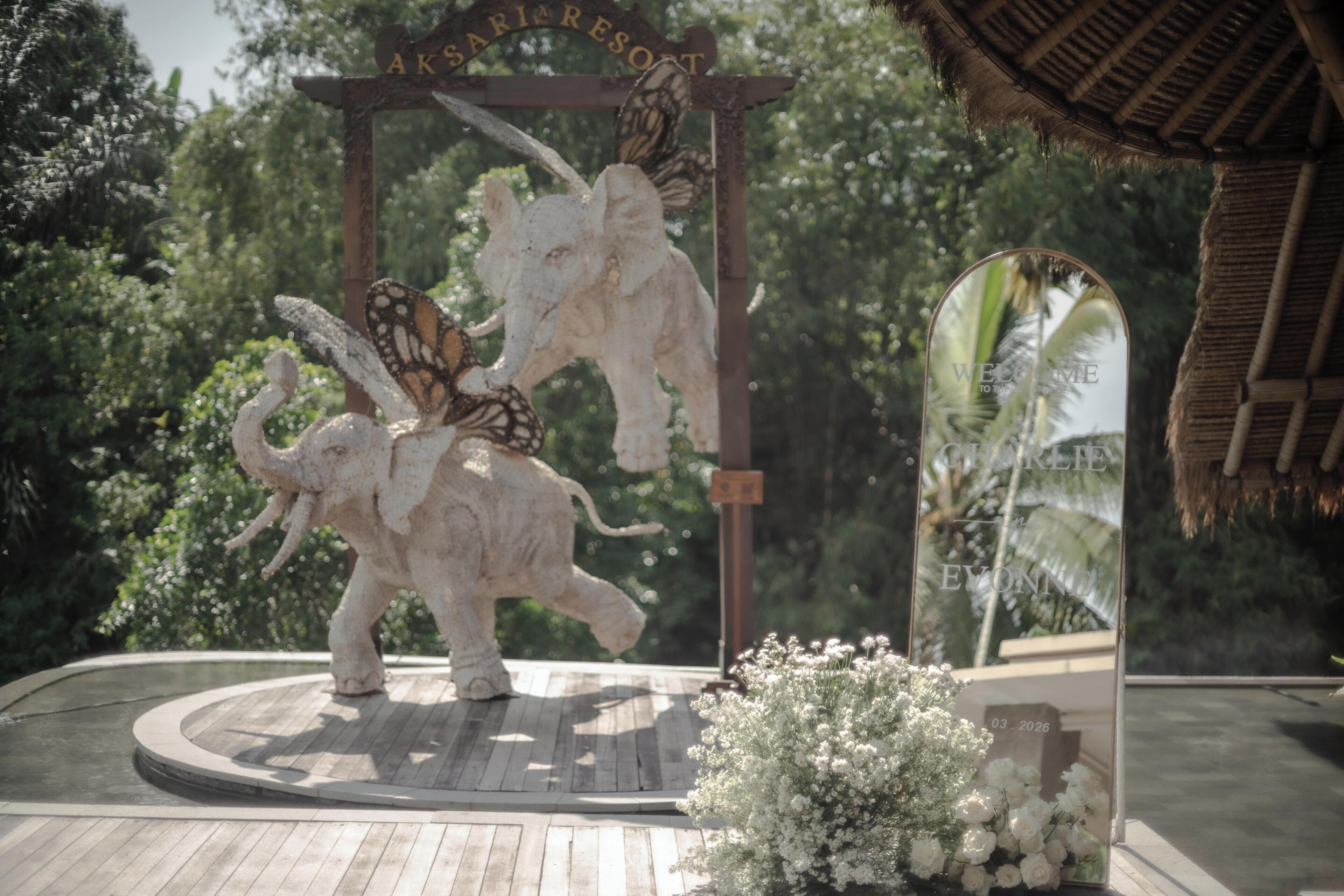 A wooden platform with a decorative elephant sculpture and a butterfly, surrounded by white flowers.