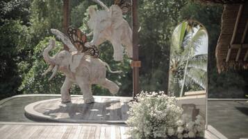 A wooden platform with a decorative elephant sculpture and a butterfly, surrounded by white flowers.