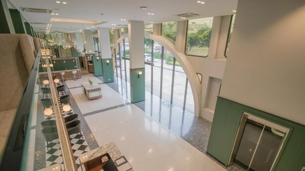 A spacious lobby with a checkered floor, seating area, and large windows offering a view of the outdoors. - Justice Hotel (Bangkok)
