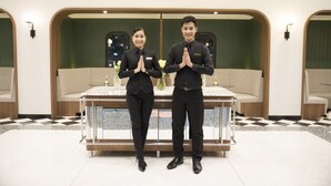 Two individuals in black uniforms standing in a modern hotel lobby with a checkered floor, a glass-top table, and a green accent wall. - Justice Hotel (Bangkok)