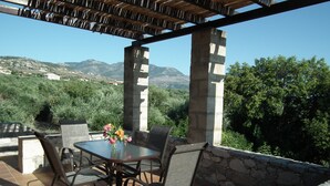 An outdoor patio with a table and chairs, a stone wall, and a view of mountains and greenery.