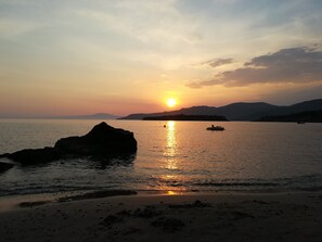 A sunset over a calm sea with a rocky outcrop in the foreground and distant hills. - First floor apartment with beautiful mountain and sea view near the sea (Στούπα)