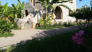 A stone building with a tiled roof, arched windows, and a gravel path leading to it.