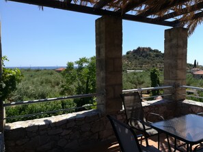 A terrace with stone walls, a glass table, and chairs, overlooking a lush landscape with trees and a distant view of a bridge. - First floor apartment with beautiful mountain and sea view near the sea (Στούπα)