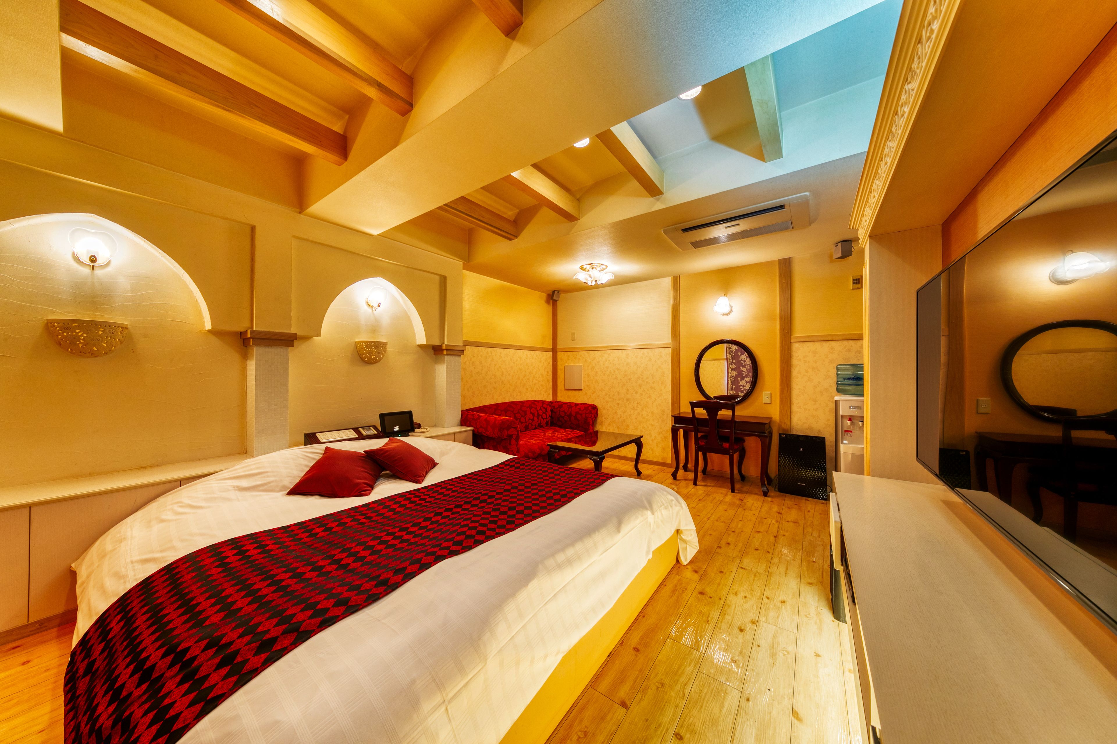 A hotel room with a large bed, a red sofa, a small table, and a mirror.