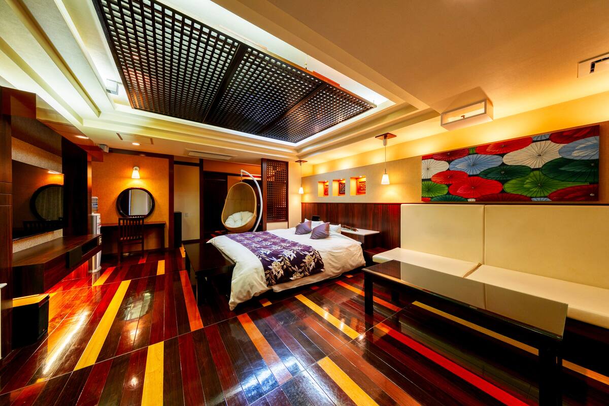 A modern hotel room with a large bed, a seating area, and a unique ceiling design.