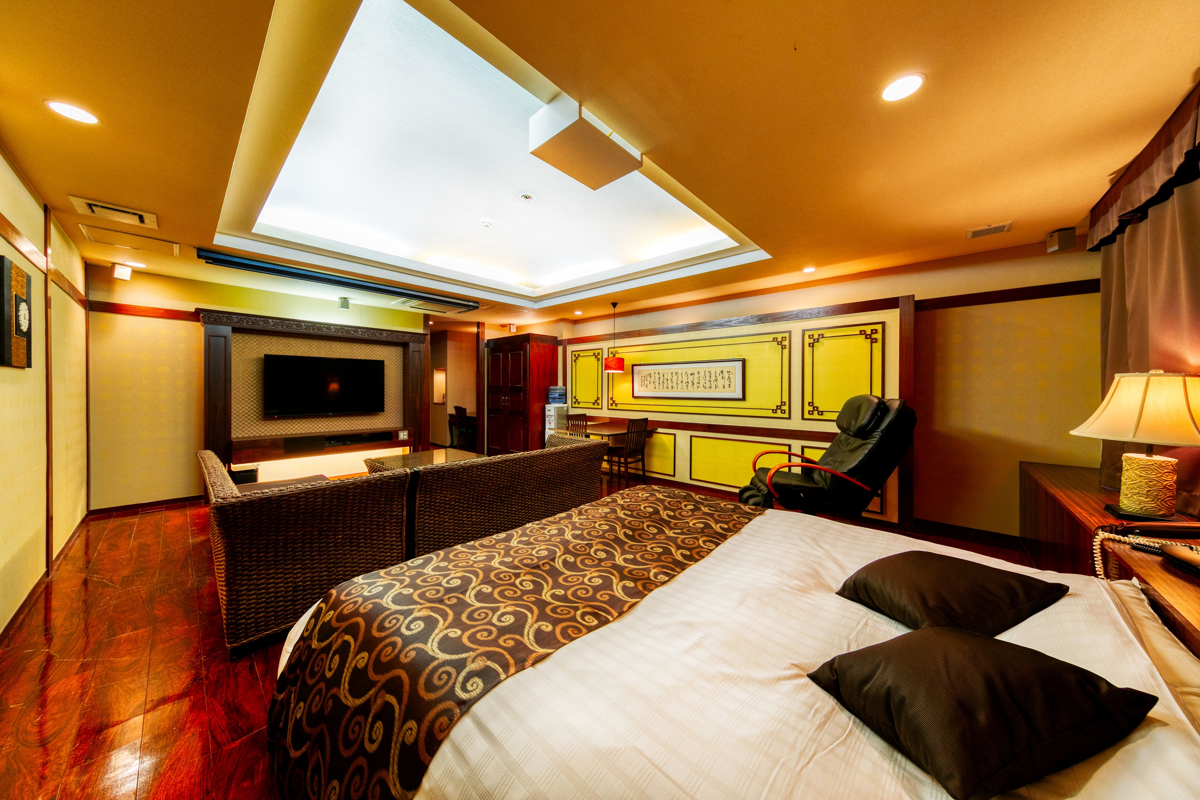 A hotel room with a large bed, a desk, a chair, a TV, and a skylight.