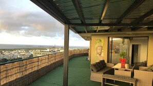Ein Balkon mit Blick auf eine Stadtlandschaft, einer Buddha-Statue und einem Tisch mit einer Pflanze.