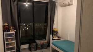 Ein Schlafzimmer mit einem Einzelbett, einem Fenster mit Vorhängen, einem kleinen Tisch mit Lampe, einem Regal mit Spielzeug und einem farbenfrohen Teppich.