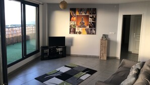 Ein Wohnzimmer mit großem Fenster, einem Flachbildfernseher, einer Couch, einem Couchtisch und einer Wand mit Buddha-Kunstwerk.